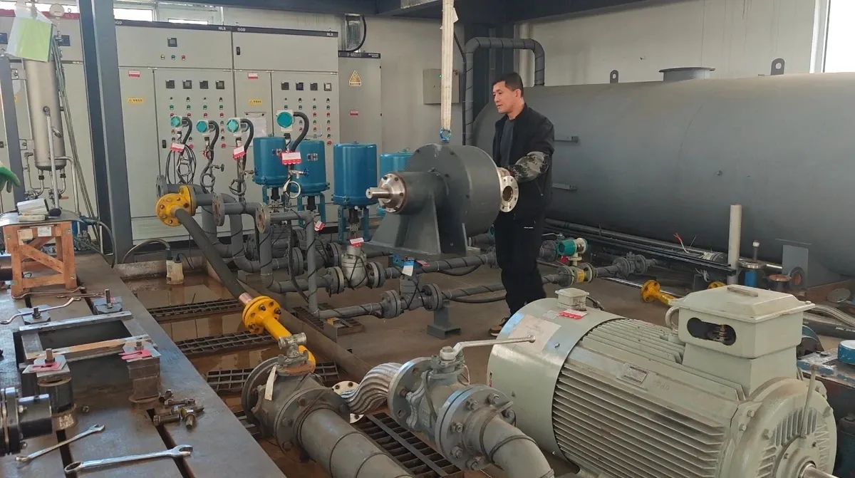 EHIK 技术人员站在泵组旁，泵组与测试台管道、流量计及控制面板相连。